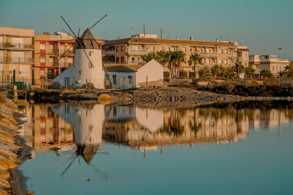 A tranquil scene of a traditional windmill and buildings reflecting in a lake in San Pedro del Pinatar, Spain.